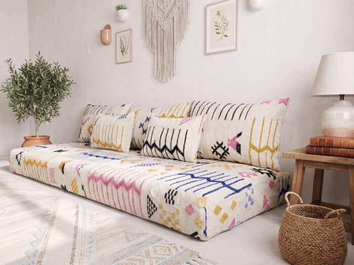 Angled view of cream floor sofa with tribal motifs beside an olive tree and terracotta pot
