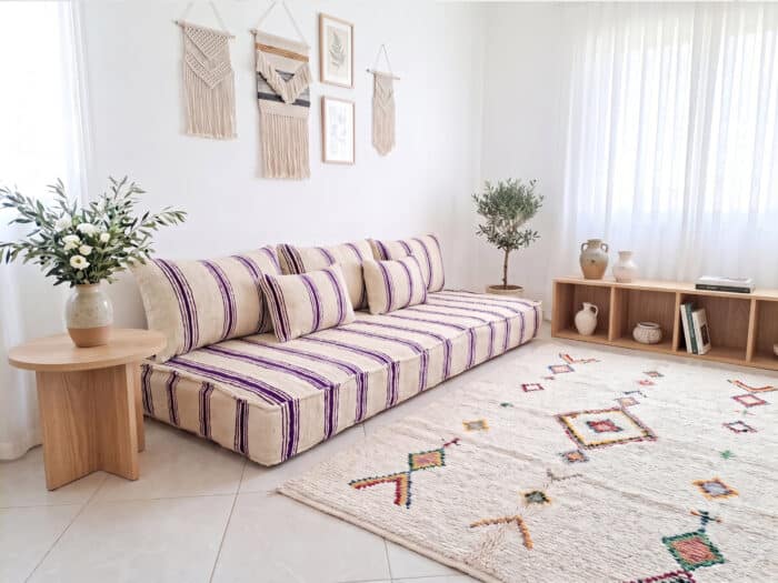 Ivory wool floor sofa with violet stripes styled in a bright Moroccan living room with olive branches and a Berber rug