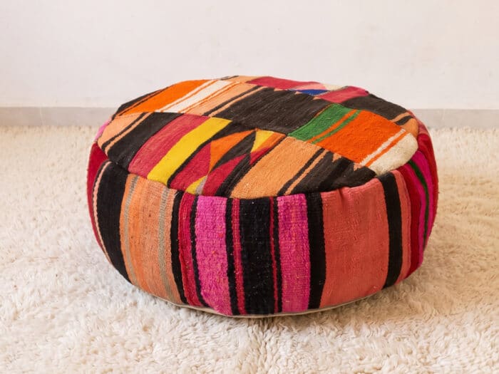 Chevron Kilim Pouf with angled orange and black striped top and terracotta sides on a cream shag rug