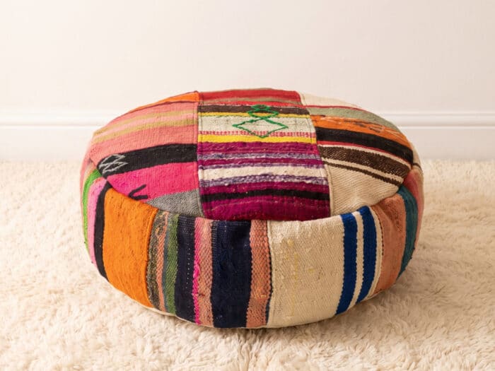 Eclectic Kilim Pouf with mixed coral and magenta patchwork top and navy striped sides on a cream shag rug