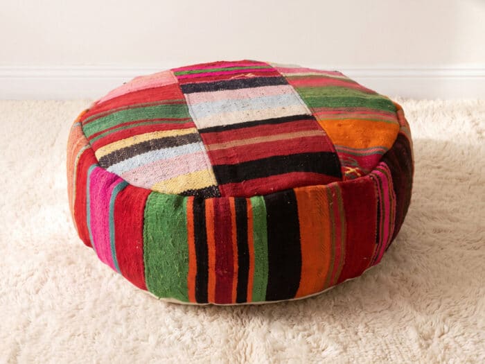 Jewel Stripe Pouf with fine multicolour candy-striped top and bold green and orange sides on a cream shag rug