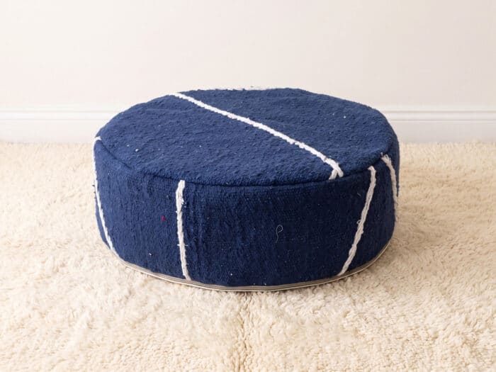 Morocco Navy Ottoman round cotton pouf styled on an ivory shag rug