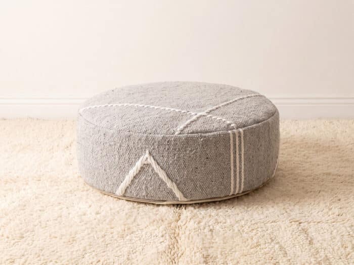 Morocco Light Grey Ottoman round cotton pouf styled on an ivory shag rug
