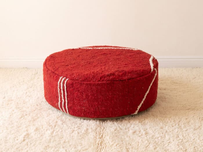 Morocco Red Ottoman round cotton pouf styled on an ivory shag rug