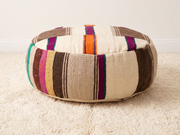 Neutral Kilim Pouf with ivory wool ground and slim magenta, teal and orange stripes on a cream shag rug