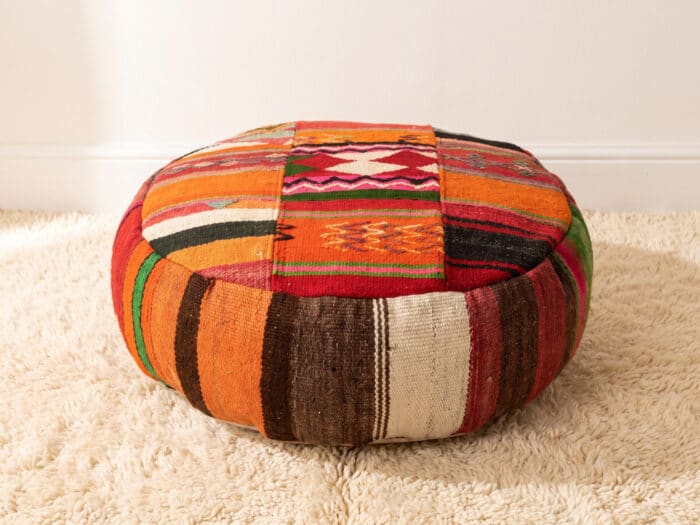 Patchwork Kilim Pouf with multicolour striped top and hand-stitched motifs on a cream Berber rug
