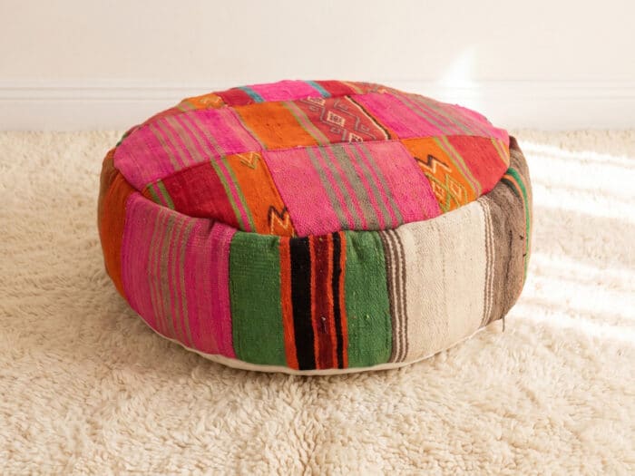 Pink Kilim Pouf with magenta and orange striped top and bold green sides on a cream shag rug