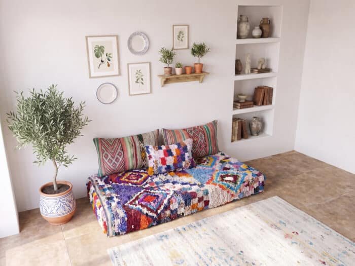 Plush boucherouite floor couch styled below a gallery wall with terracotta pot and alcove shelves
