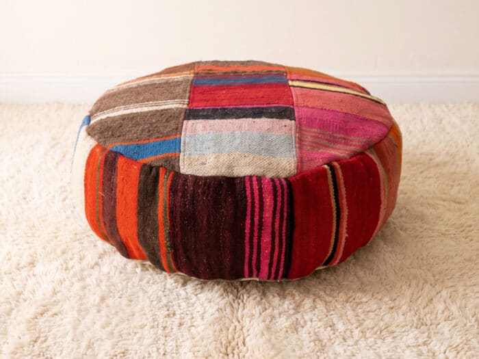 Striped Patchwork Pouf with bold red and pink side stripes and a pastel kilim top on a cream shag rug