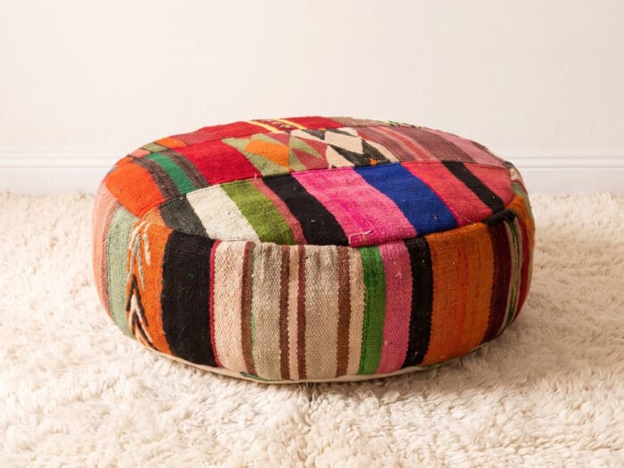 Vibrant Floor Pouf with bold multicolour kilim stripes and diamond motifs on a cream shag rug