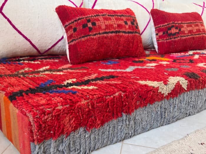 Vintage red wool floor sofa with symbols shown close-up with red kilim and cream cushions