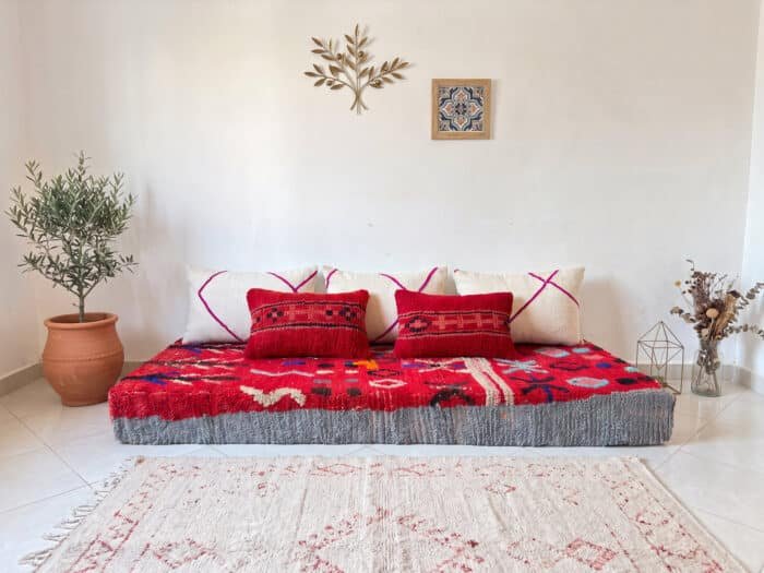 Vintage red wool floor sofa with symbols styled in a bright room with olive tree and terracotta pot