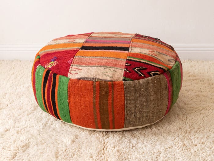 Warm Stripe Pouf with coral and cream striped top and bold green sides on a cream shag rug