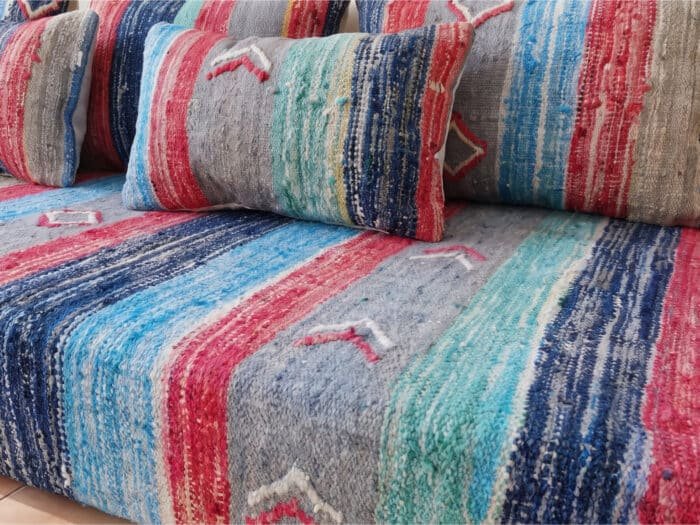 Close-up of the boucherouite floor sofa in upcycled cotton, showing raspberry diamond motifs and blue stripes