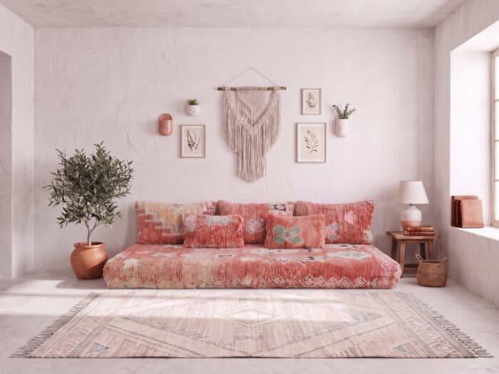 Blush pink shag floor sofa styled below macrame and olive tree on a whitewashed wall
