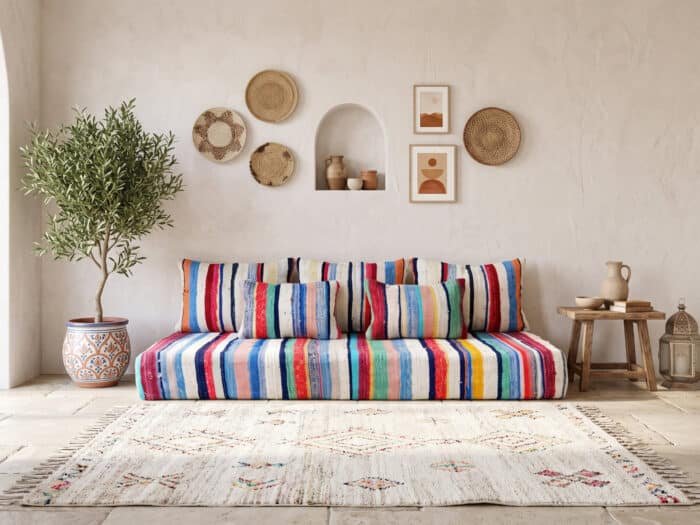 Multicolor boho floor sofa styled against a white plaster wall with striped cushions and olive tree