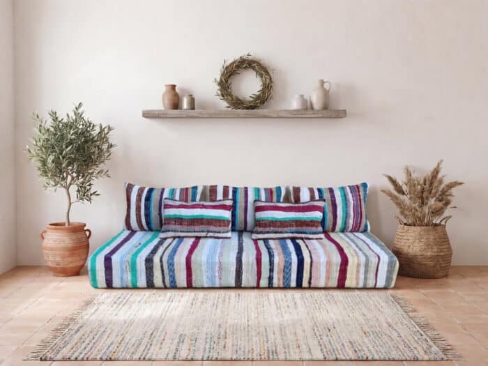 Pastel stripe floor sofa styled with a rag rug and olive tree against a whitewashed wall