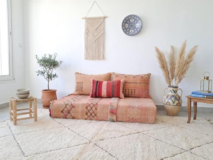 Pink Mellali floor sofa, 120 cm, in a bright room with macramé hanging and Moroccan plate