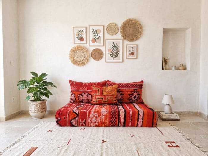Scarlet floor couch against a white wall with straw wall baskets, monstera plant and ivory rug